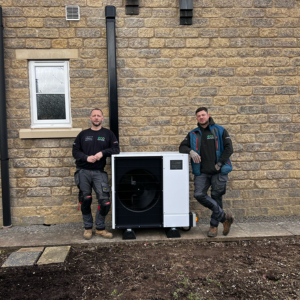 Air Source Heat Pump up against a wall with 2 members of eco partners staff.