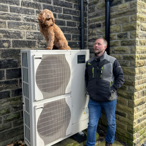 Air source heat pump with a man stood at the side and a cockerpoo dog sat on top.