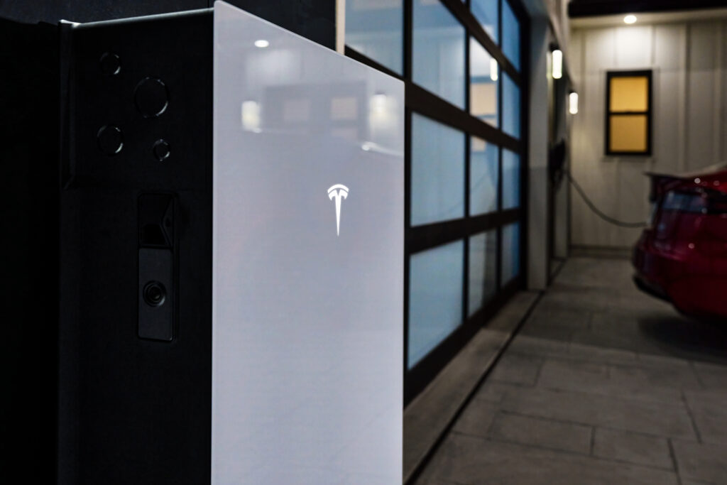 An image of a Tesla Powerwall 3 with a garage door in the background.