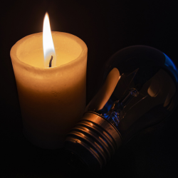 Image of a candle lit with a lightbulb laid next to it. Signifying a power cut.