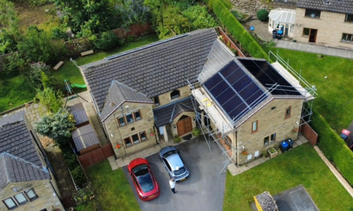 Birds eye image of a detached house roof with in roof solar panels. 2 Cars parked on the drive.