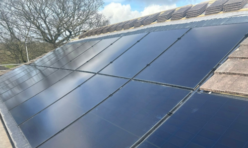 A close-up image of in roof solar panels on a roof. A tree and blue sky with white clouds in the background.