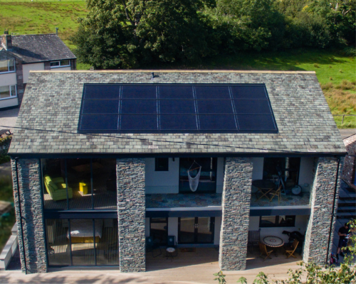 An image of a modern house with glass and stone facia. The stone roof has integrated Solfit solar panels.